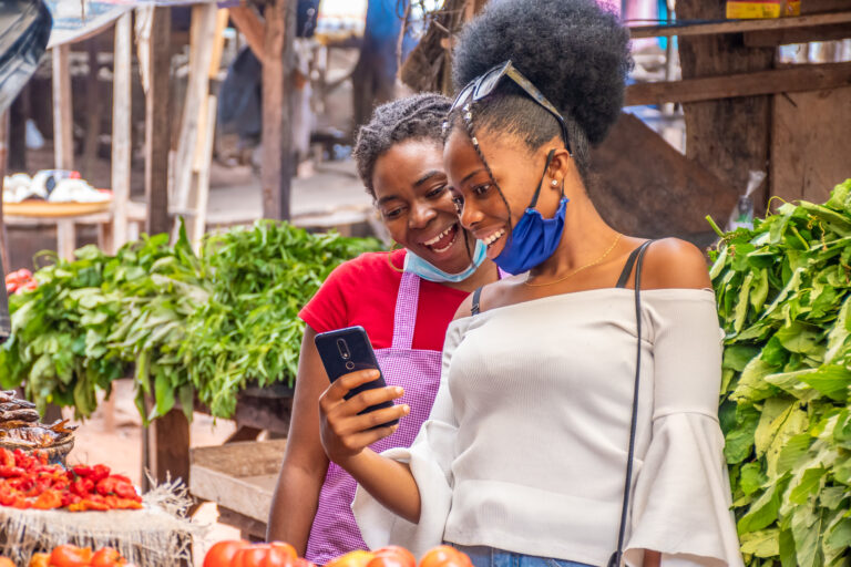 Two women viewing content on a phone in a local African market